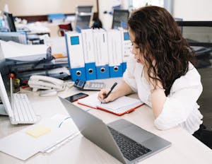 Woman Writing on Notebook While Using Laptop