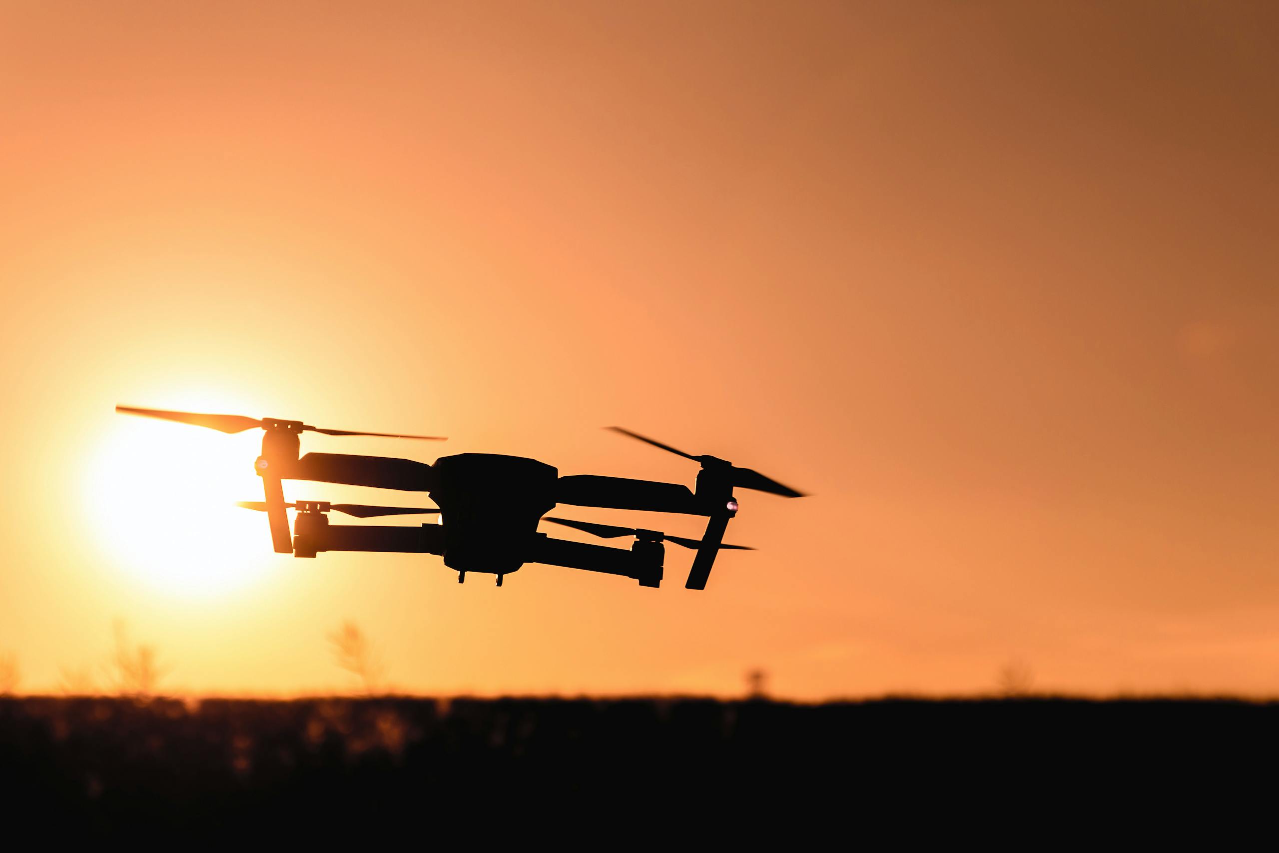 A drone in silhouette against a vibrant orange sunset sky, showcasing modern technology and aerial photography.