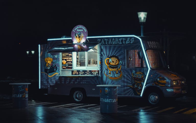 Colorful food truck glowing with neon lights during nighttime.