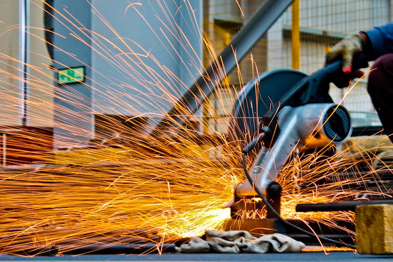 A worker operates a grinder cutting metal, creating a vibrant display of sparks in an industrial setting.