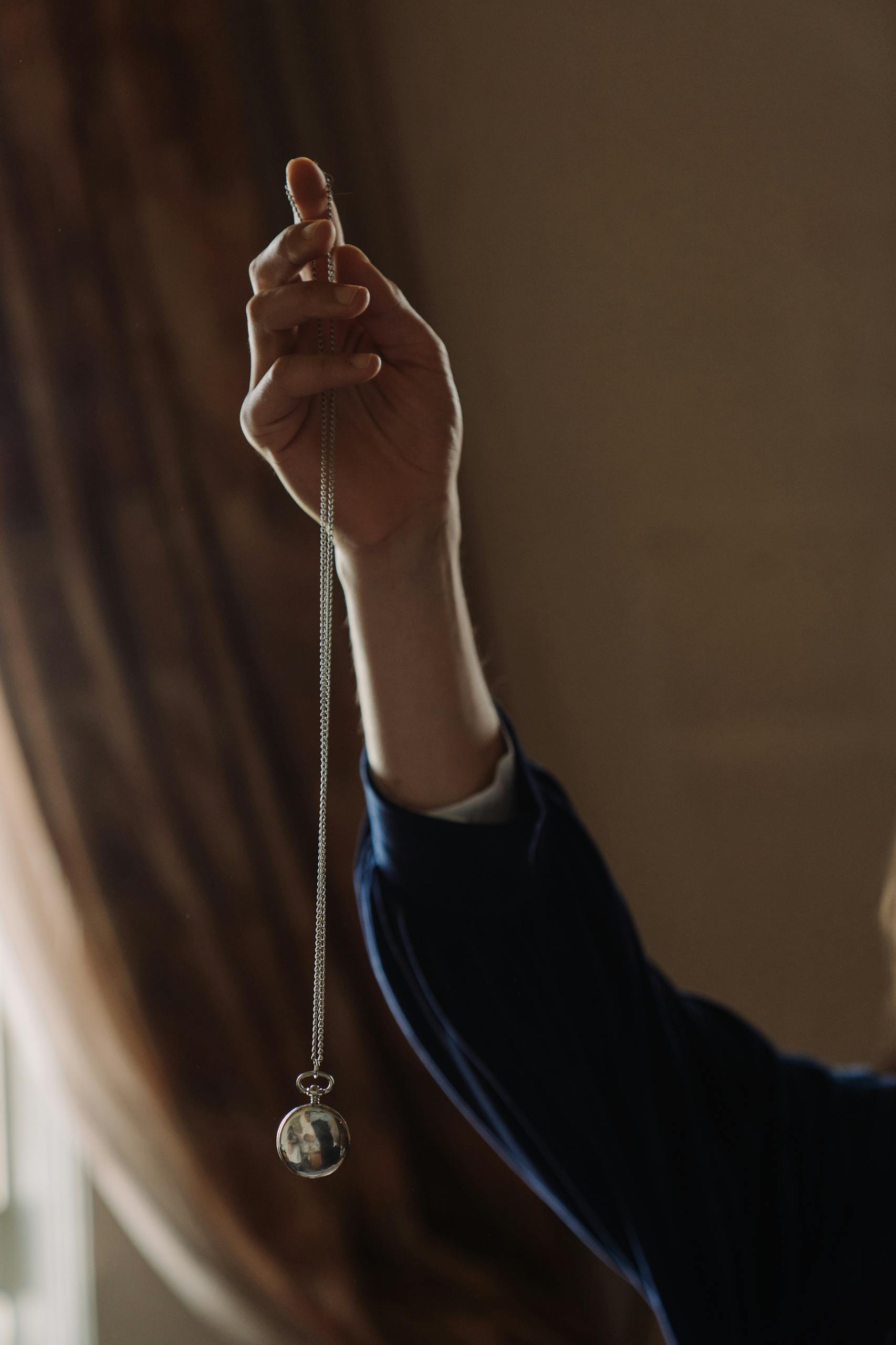 A male hand elegantly holding a silver pocket watch chain, symbolizing time's flow.